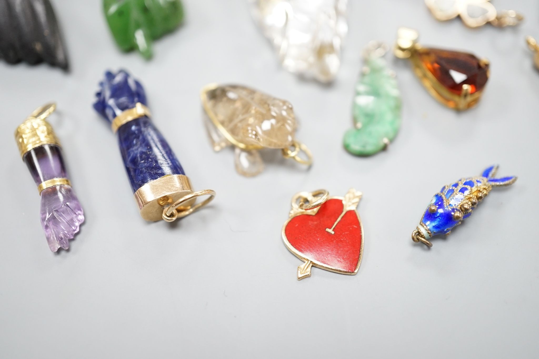 Seven assorted yellow metal or gilt metal mounted clasped hand charm or pendants, largest, 94mm, and seven other smaller charms/pendants including 14k and red enamel heart and an enamelled articulated fish.